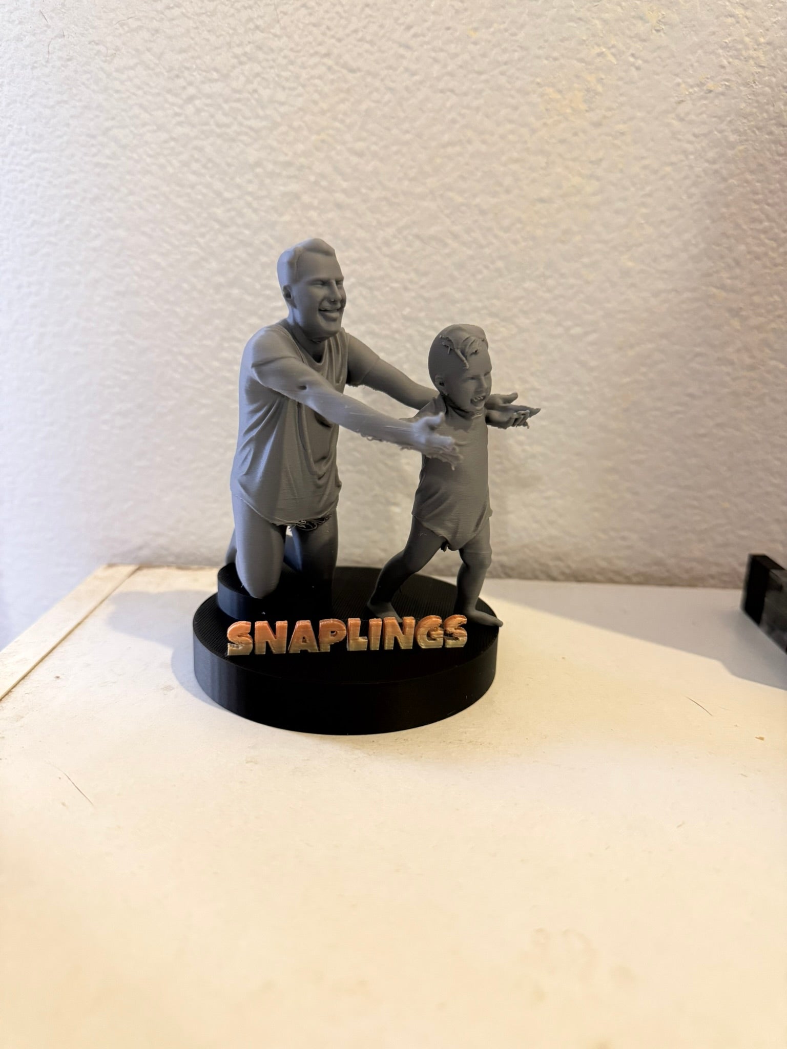 Statue of two people embracing with 'SNAPLINGS' branding on a white surface.